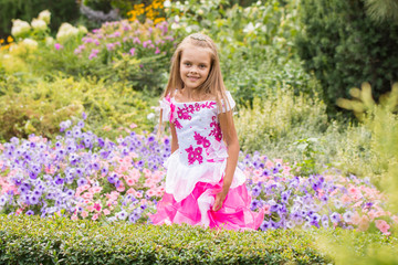 Happy little girl in a long dress at flower bed
