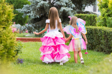 Two little girls, princess and fairy strolling through the garden