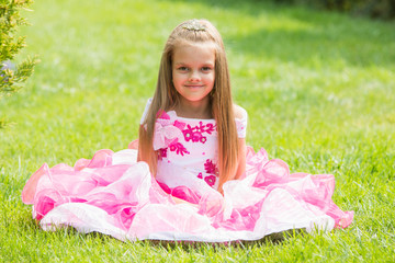 Five-year girl in a beautiful dress sat on the lawn in the green garden