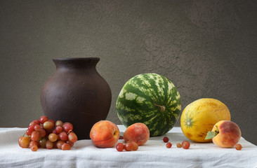 Obraz na płótnie Canvas Глиняный кувшин и фрукты: виноград, дыня, арбуз и персики.