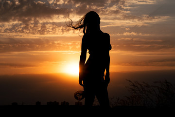 Young girl silhouette with shawl on background of beautiful cloudy sky with golden red sunset and rays of light