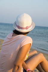 Fototapeta na wymiar Girl brunette in white hat looking at sea while sitting on beach