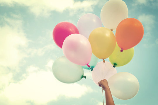 Girl hand holding multicolored balloons done with a retro vintage instagram filter effect, concept of happy birth day in summer and wedding honeymoon party (Vintage color tone)