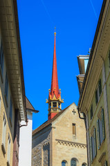 Red top of famous church between buildings and blue sky in downtown Zurich, Switzerland.