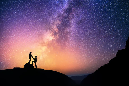 Love is in the air.Romantic couple standing together holding hands in the mountains. Beautiful Milky Way galaxy on the background.