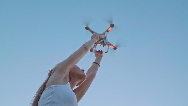 SLOW MOTION 240 fps: Drone is taking off from woman's hands. Young woman releasing copter to fly in the sunset field. Modern technology in our life. 