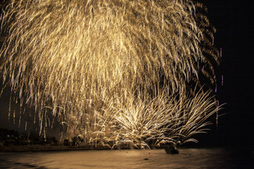 Golden fireworks falling over sea with reflections