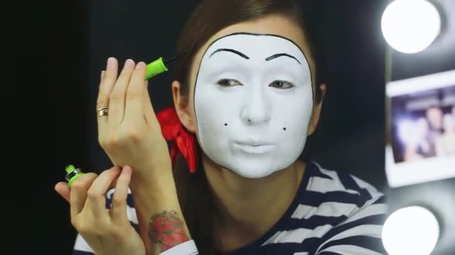 Woman mime does makeup near the mirror