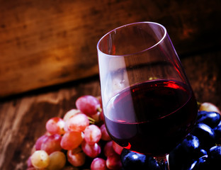 Red wine and blue and pink grapes on a dark wooden background, t
