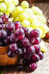 Purple round ripe grapes in a wicker basket on an old wooden bac