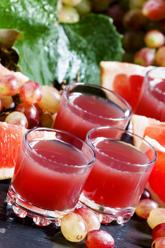 Fresh juice of red grapes and grapefruit on a dark background, s