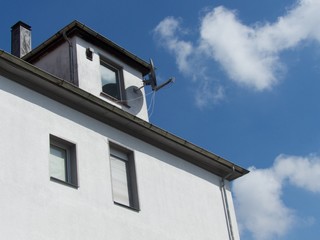 Schneeweiße Fassade mit Mansarde, Dachgaube und Satellitenschüssel vor blauem Himmel im...