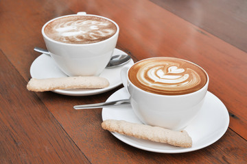 two cups of latte art coffee in a white cup on wooden background