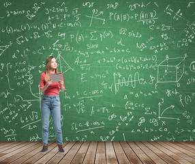 Young lady is pondering about complicated math problem. Formulas and graphs are drawn on the green...