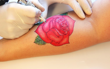 tattooer showing process of making a tattoo on young  woman hand. Tattoo design in the form of rose