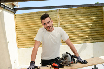 handsome young man carpenter working with electric tool on wood timber in construction site
