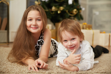 Cheerful girl and boy lying on the floor near a Christmas tree