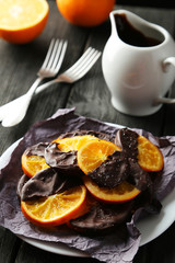 Delicious slices of orange coated chocolate on plate on black wooden background