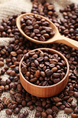 Fototapeta premium Coffee beans in wooden spoon and bowl on a sack, close up