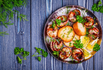 Fried snails with garlic butter and herbs on dark background