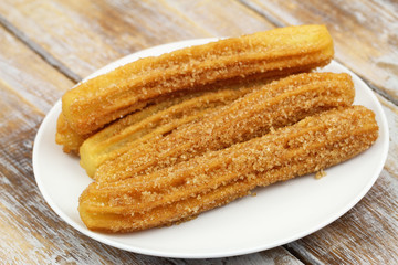 Churros on white plate on rustic wooden surface
