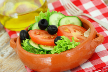 Salad with lettuce, tomatoes, cucumber and black olives in clay bowl
