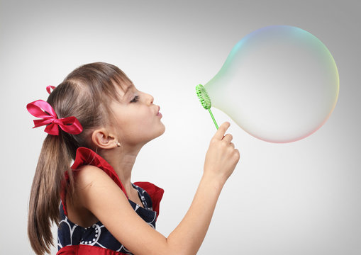 Portrait of funny child girl blowing big soap bubble, studio sho