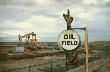 aged and worn vintage photo of oil field sign with derrick in background