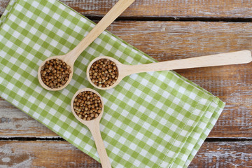 Coriander seeds on wooden spoons on checkered cloth
