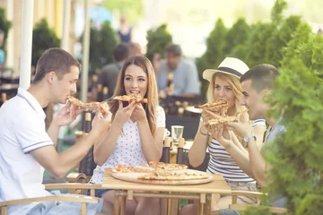 Foto op Canvas Group of four young people eating pizza in a restaurant © bokan