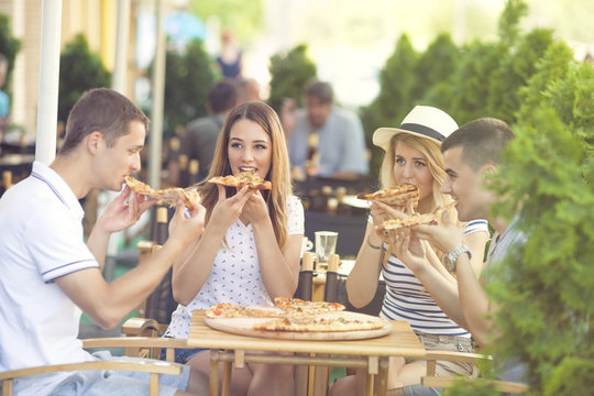 Group of four young people eating pizza in a restaurant