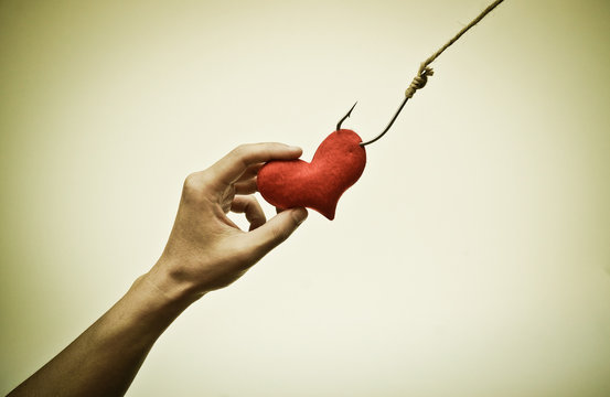 hand trying to catch a red heart on a fish hook - Love trap concept
