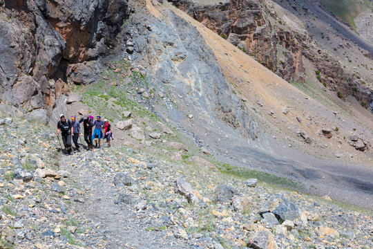 Group of Climbers Hard Walk Hiker Team Scramble Up on Rocky Trail with Severe Colored Steep on Background