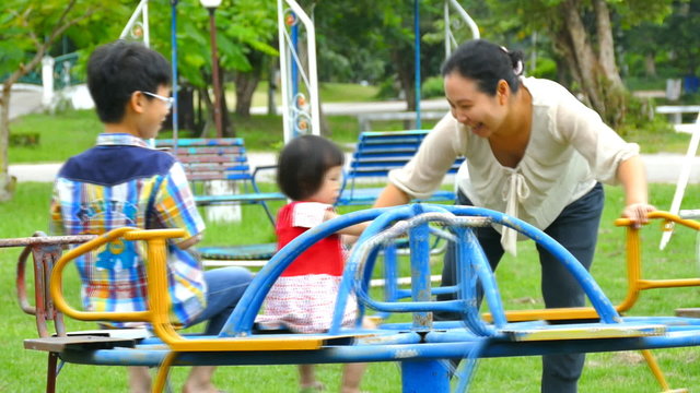 Mother rolls her children on the carousel at the playground in the park 