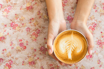 Vintage woman hands holding latte art coffee mug on flower vinta
