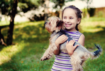 little girl in a striped sweater smiles and holds a small dog