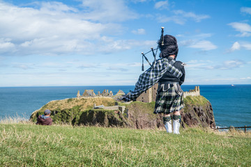 Traditional scottish bagpiper in full dress code at Dunnottar Castle in Stonehaven