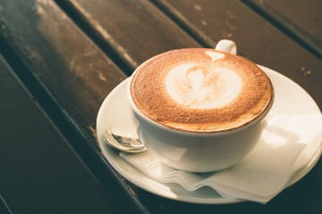 White cup of cappuccino with cinnamon on a wooden table in a caf