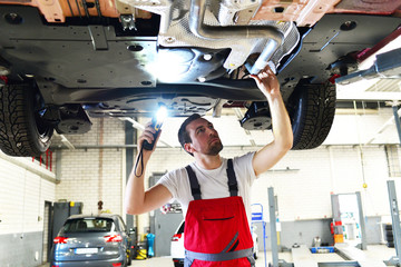 Mechaniker in einer Werkstatt kontrolliert den Unterboden eines Autos // mechanic in garage checked...