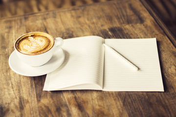 Cup of coffee and blank diary with a pencil on a wooden table