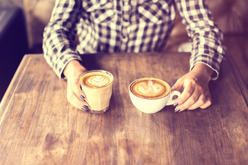 Hipster girl holding two cups of coffee on a wooden table