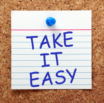 The phrase Take It Easy in blue text on an index card pinned to a cork notice board as a reminder that we have to be mindful about time out to relax and be calm