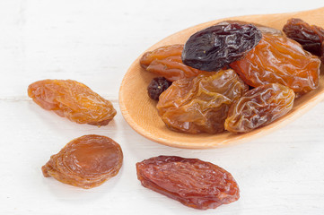 Raisins in wooden spoon on white wood background
