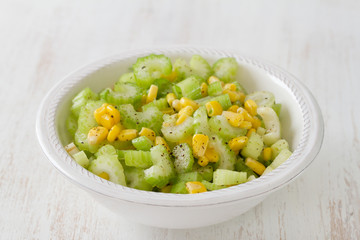 salad celery with corn in white bowl on white wooden background