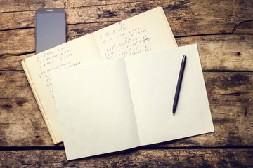 Exercise book with smartphone and pen on old wooden table