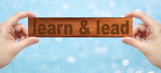 Hands holding a wood engrave with word learn and lead