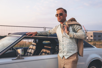 Retro 1970s fashion man leaning with arm on roof of vintage car.