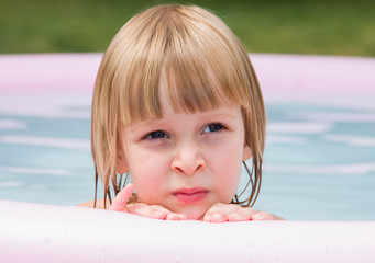 Thoughtful little girl in inflatable pool at summer day
