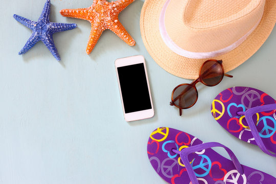 colorful flip flops, starfish, cellphone, fedora hat and sunglasses on wooden background
