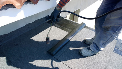 Roofer preparing part of bitumen roofing felt roll for melting by gas heater torch flame